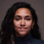 A headshot of me, with my hair down and smiling at camera. Standing against a grey backdrop.